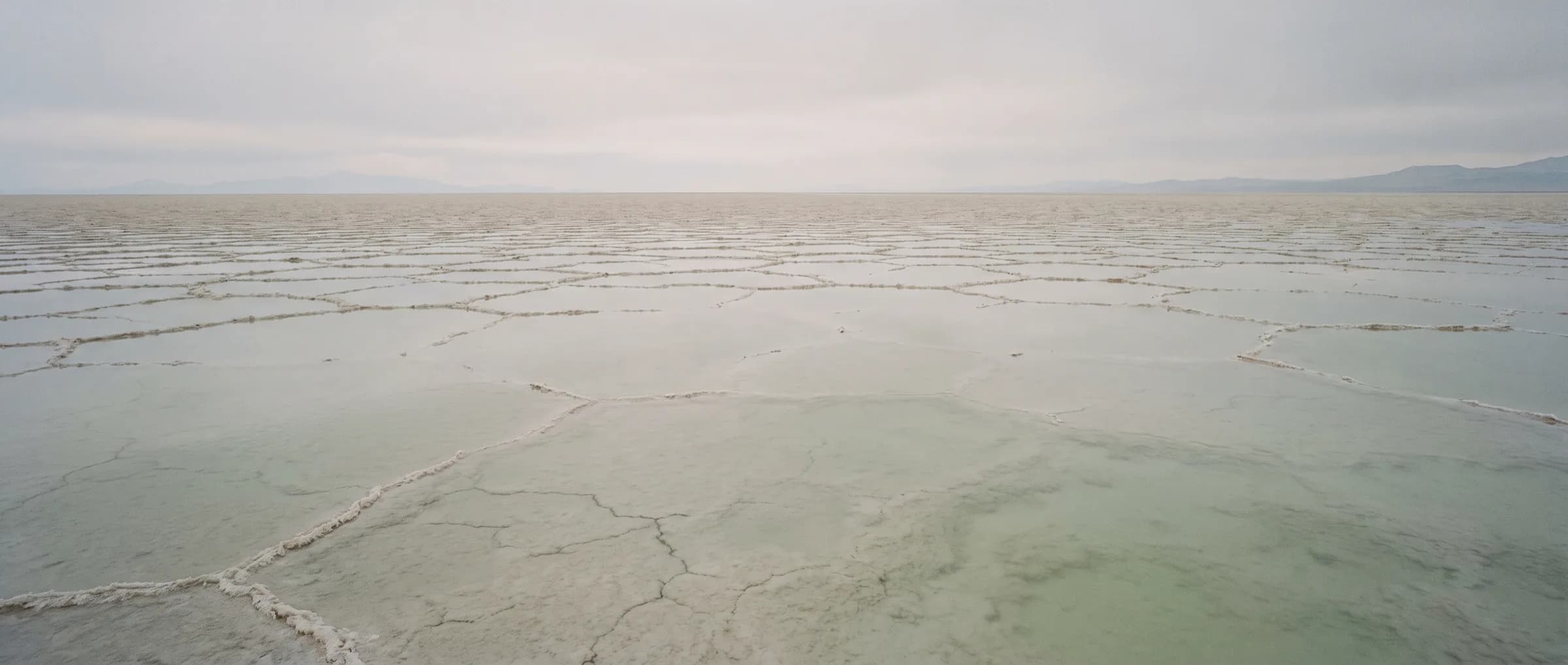 A shallow sheet of water over cracked mineral salt flat at dawn
